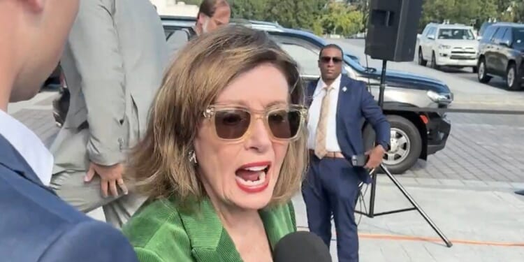 Nancy Pelosi speaking to the media while surrounded by security and vehicles, showcasing her engagement in a public event.