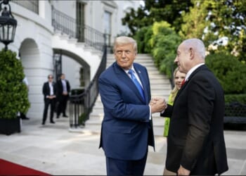 Donald Trump and Benjamin Netanyahu shake hands outside the White House, surrounded by greenery and security personnel, during a diplomatic meeting.
