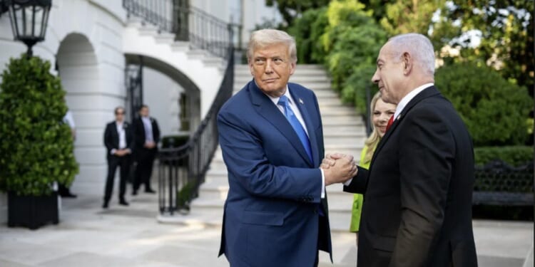 Donald Trump and Benjamin Netanyahu shake hands outside the White House, surrounded by greenery and security personnel, during a diplomatic meeting.