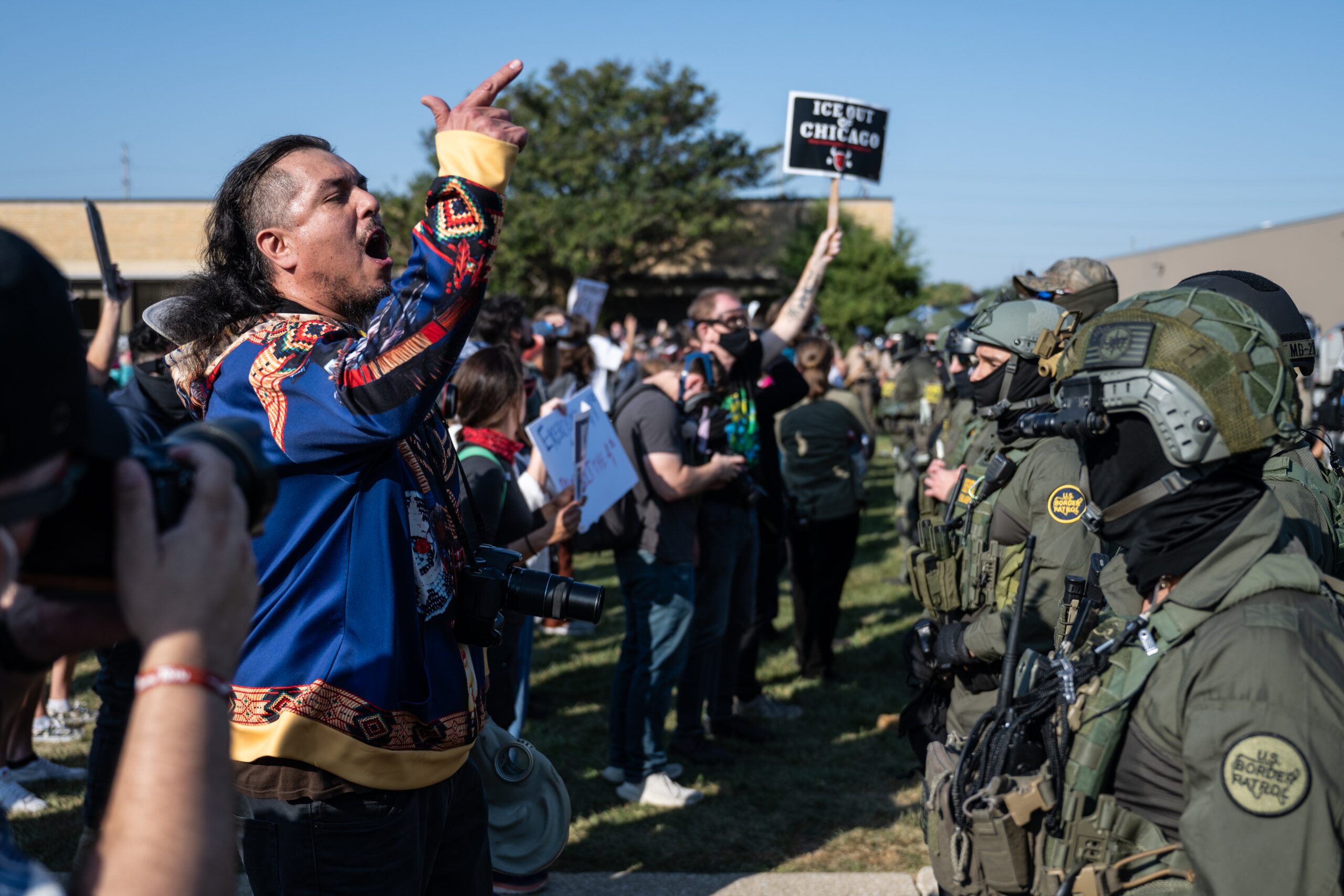 Protester passionately gestures during a demonstration against police presence, with law enforcement in tactical gear visible in the background.