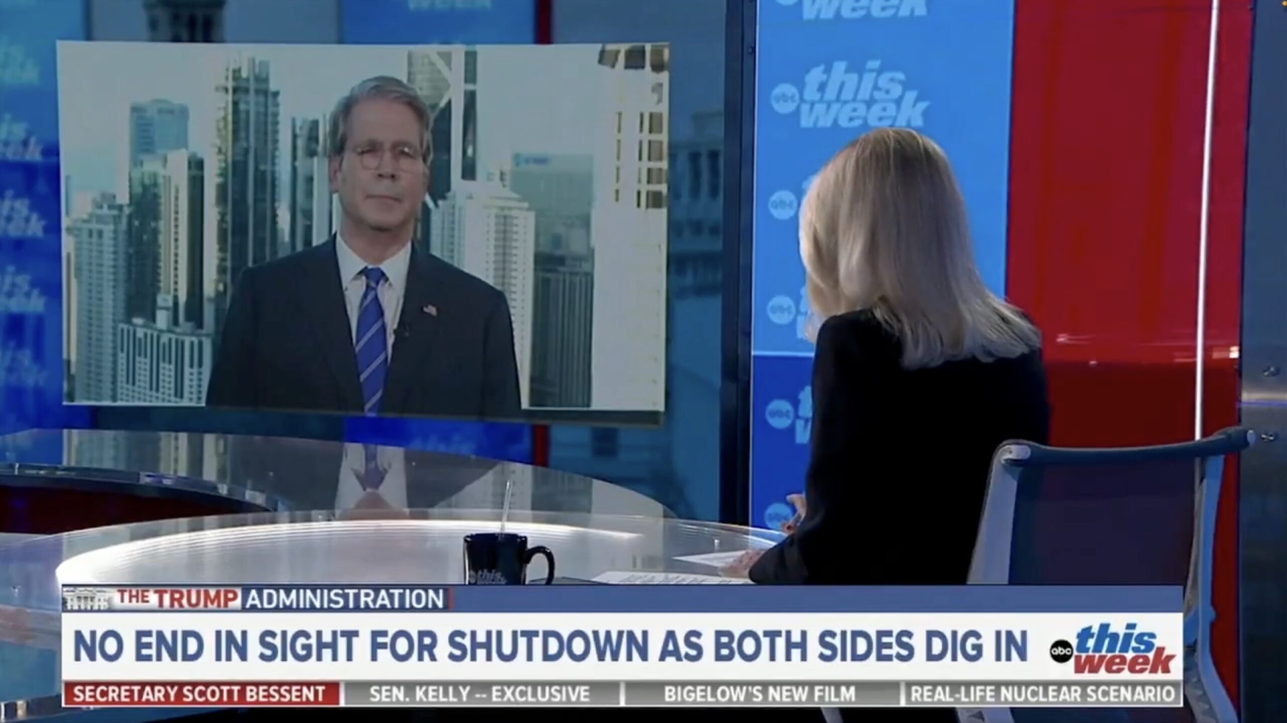 Discussion on government shutdown tensions featuring a guest speaker on a news program, with a backdrop of a city skyline.