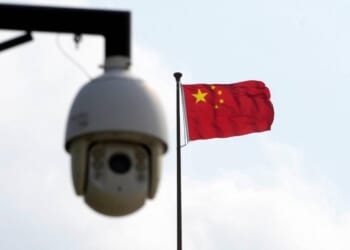 Chinese flag waving in the background with a surveillance camera in the foreground, symbolizing security and monitoring in China.