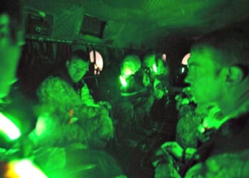 Soldiers seated inside a military aircraft, illuminated by green lights, preparing for a night operation.
