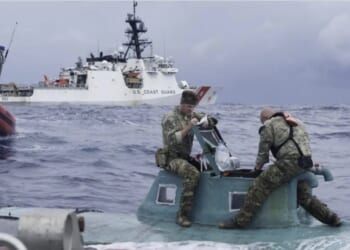 U.S. Coast Guard personnel inspect a small vessel at sea, with a larger Coast Guard ship in the background, showcasing maritime operations and rescue efforts.