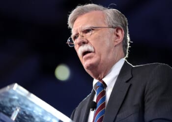 John Bolton speaking at a podium during a public event, emphasizing key political points with a serious expression.