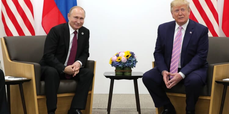 Russian President Vladimir Putin and former U.S. President Donald Trump meet for a discussion, with national flags in the background and a floral arrangement on the table.