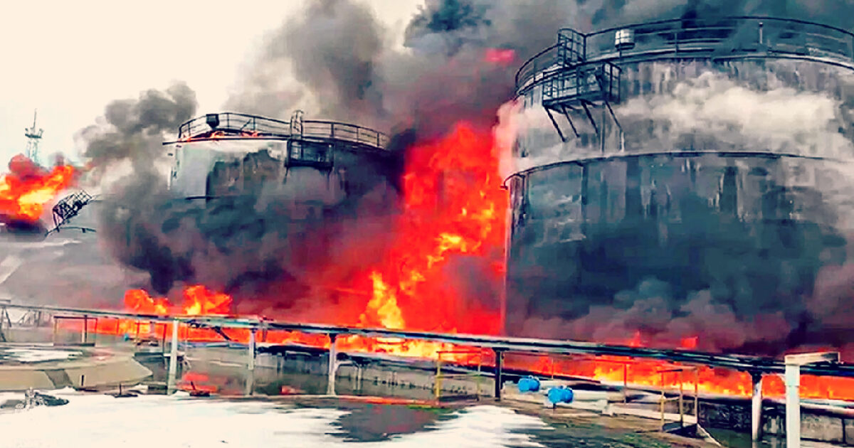 Industrial storage tanks engulfed in flames and smoke during a fire incident, showcasing the intensity of the blaze and surrounding damage.