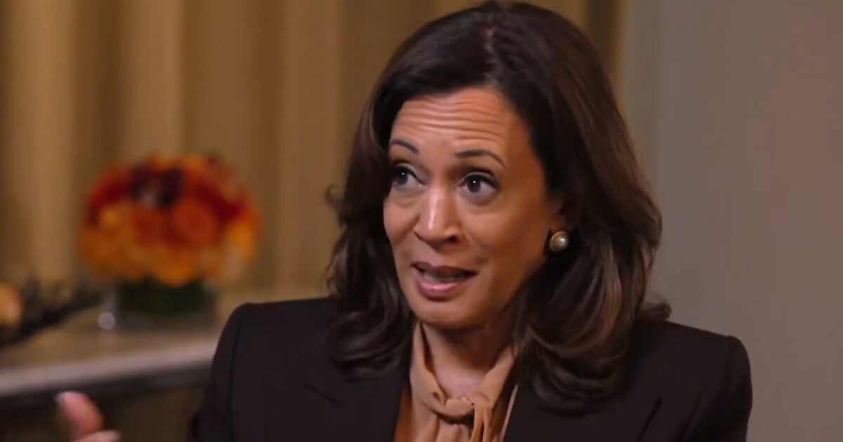 A woman with long, dark hair and a brown blouse engages in conversation, expressing her thoughts with animated gestures against a softly blurred background.