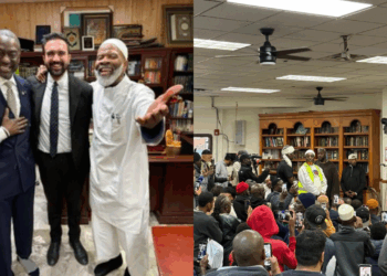 Group of men smiling together in an office setting, with a crowd gathered in a community space, highlighting engagement and connection among diverse individuals.