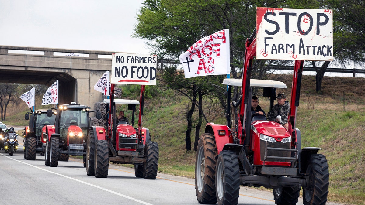 A line of tractors and vehicles moves through a rural landscape toward a hillside covered in white crosses.