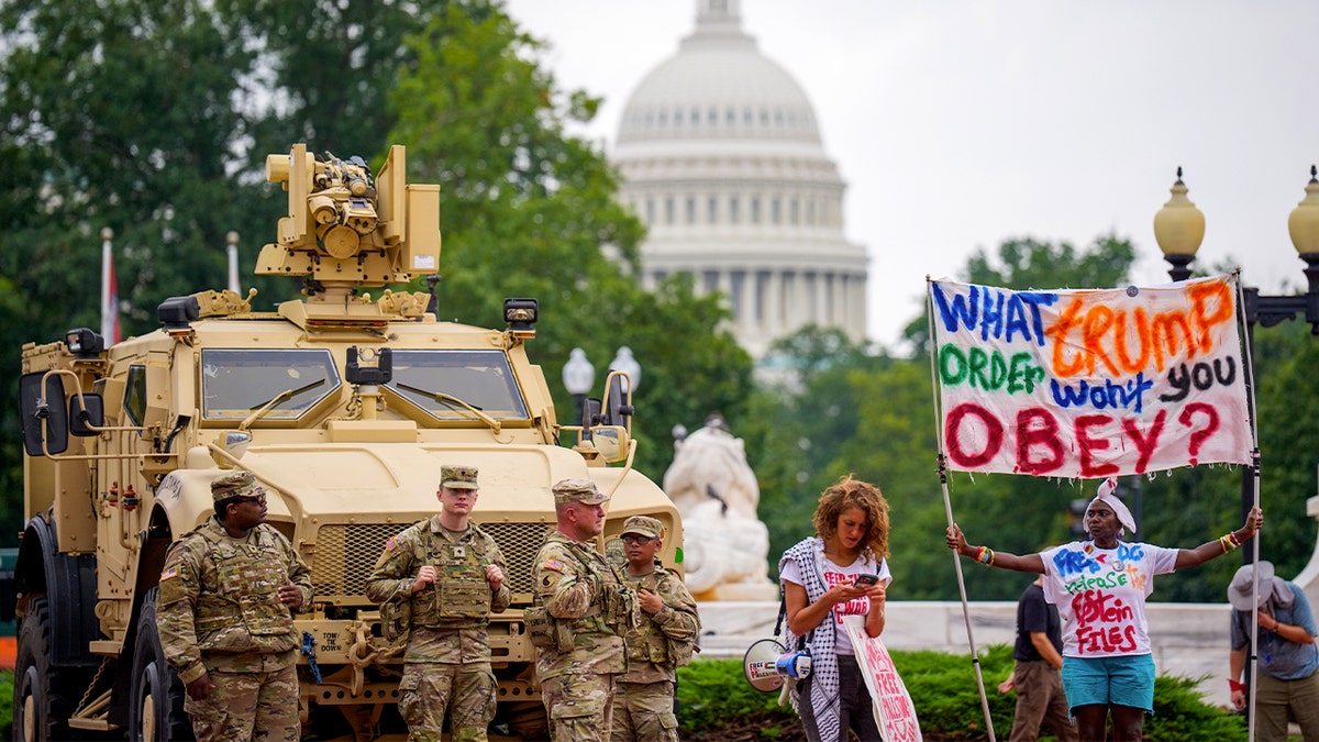 Soldiers stand next to protester holding a sign that reads "What Trump Order Won't You Obey?"