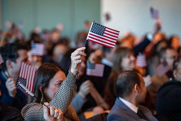 People wave U.S. flags to celebrate becoming U.S. citizens after taking the oath of allegiance during a naturalization ceremony
