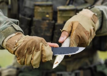 A young soldier cutting a wooden stick with a knife.