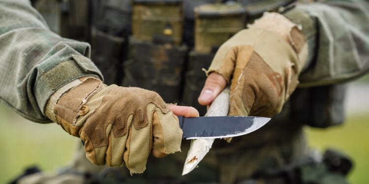 A young soldier cutting a wooden stick with a knife.