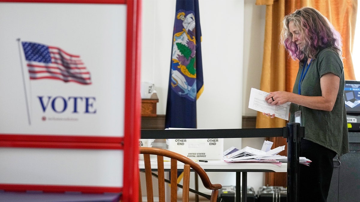 An election worker handling and sorting envelopes on a table.