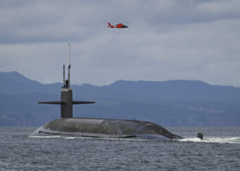 A U.S. Coast Guard MH-65E Dolphin helicopter flies over the Ohio-class ballistic-missile submarine USS Maine (SSBN 741) as it transits the Strait of Juan de Fuca off the Washington Coast, March 18, 2025, during routine operations.