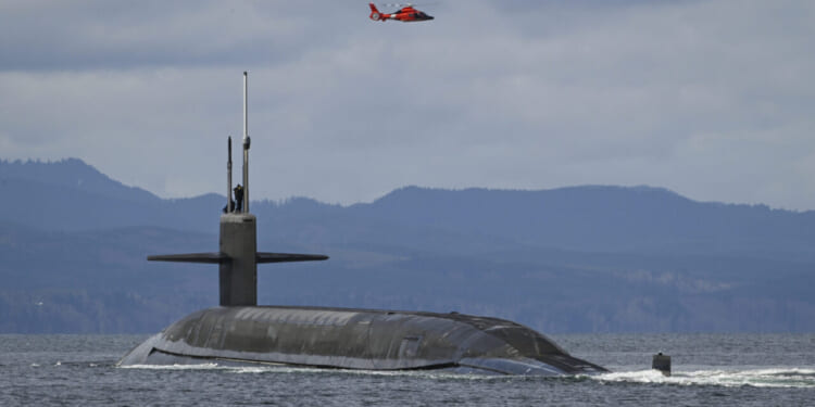 A U.S. Coast Guard MH-65E Dolphin helicopter flies over the Ohio-class ballistic-missile submarine USS Maine (SSBN 741) as it transits the Strait of Juan de Fuca off the Washington Coast, March 18, 2025, during routine operations.