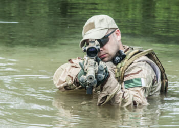 Member of Navy SEAL Team crossing the river with weapons drawn.