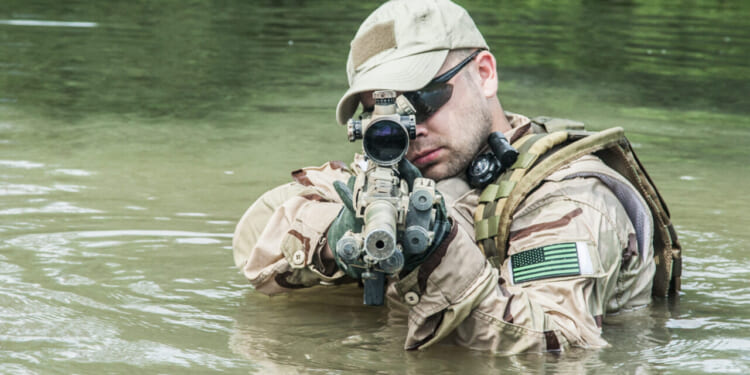 Member of Navy SEAL Team crossing the river with weapons drawn.