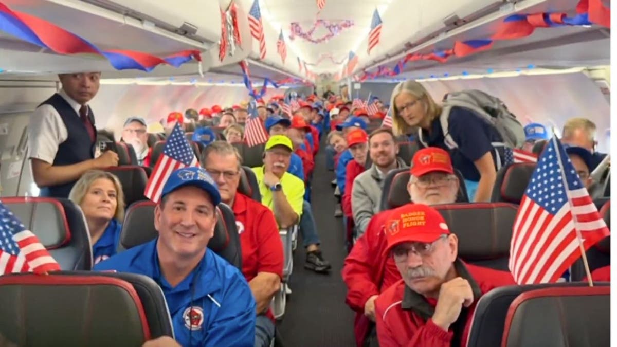 Rows of Honor Flight veterans holding small American flags inside an airplane cabin