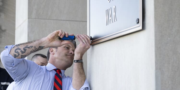 Pete Hegseth screwing a plaque in at the Pentagon.
