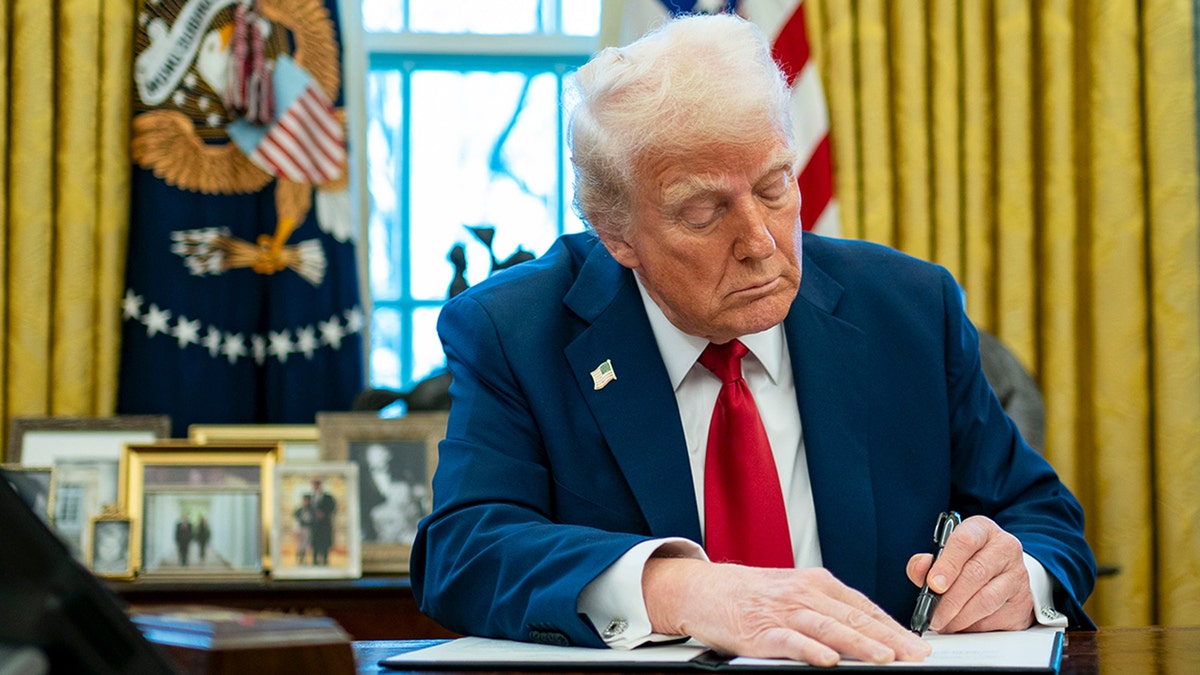 President Donald Trump signs a document in the Oval Office.