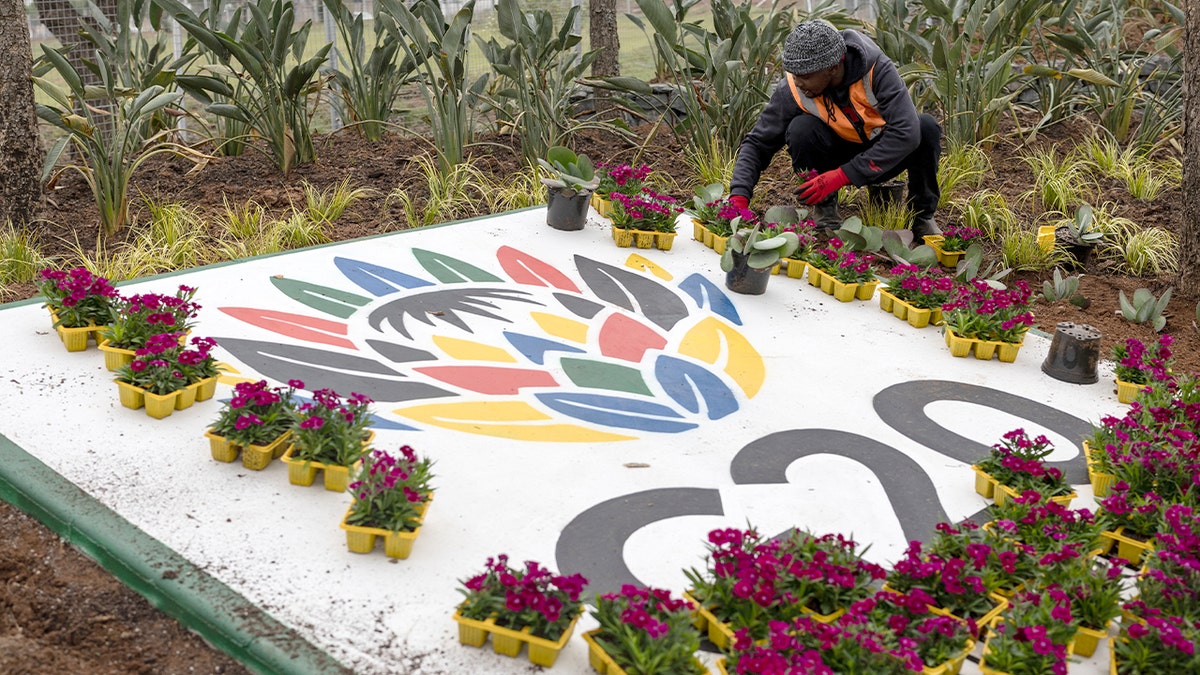 A worker arranges colorful flowers near a large event logo in South Africa.