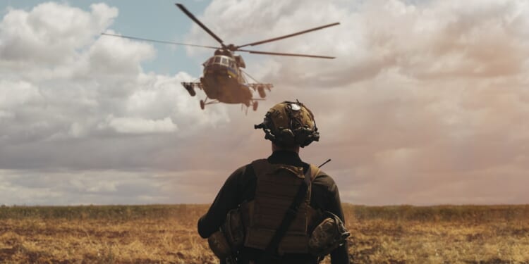 Soldier in tactical gear observing military helicopter landing in open field