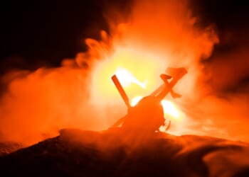 A crashed helicopter at night, with flames in background.