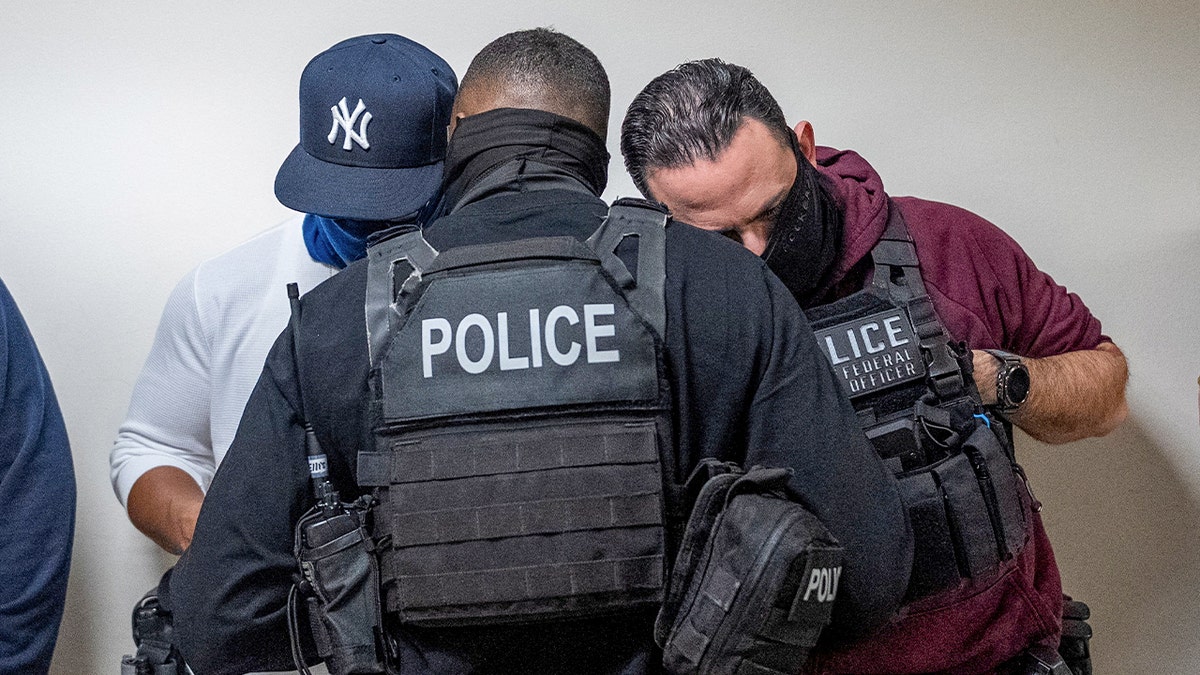 Person wearing "Police" vest confers with two masked individuals