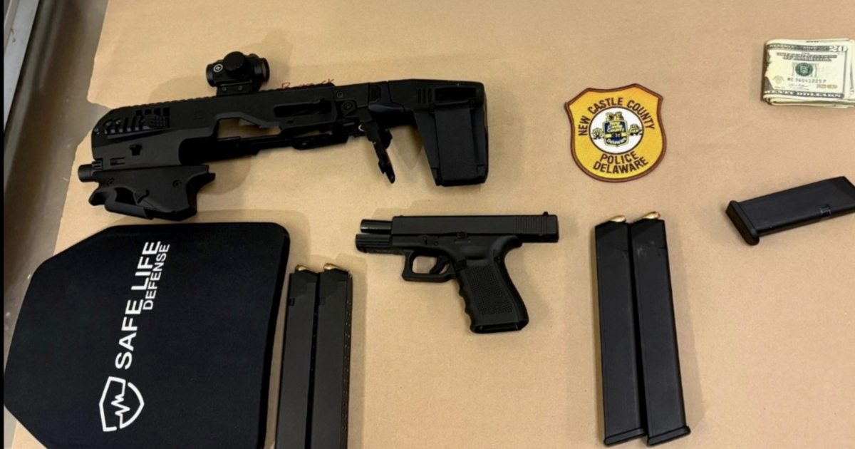 Image shows a tactical shotgun, a handgun, ammunition magazines, a ballistic shield, cash, and a police badge on a countertop.