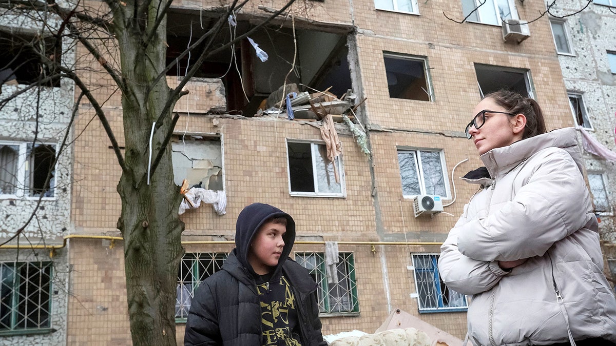 People in Ukraine stand next to damaged building