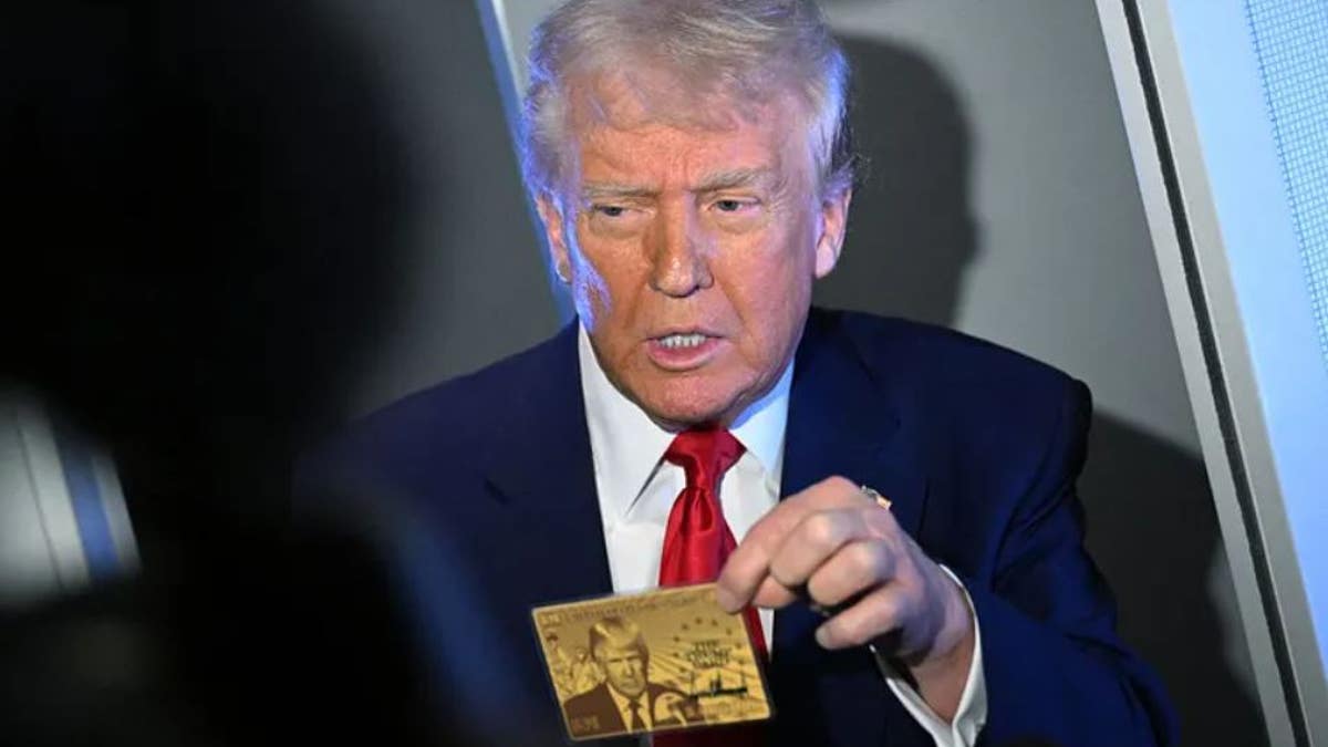 President Donald Trump holds the $5 million dollar Gold Card as he speaks to reporters while in flight on board Air Force One.