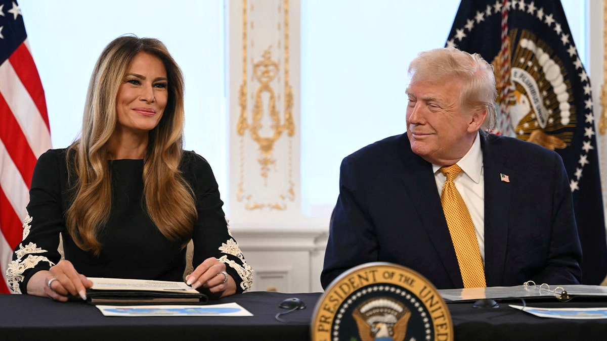 First lady Melania Trump smiles while sitting next to President Donald Trump, who is smiling at her