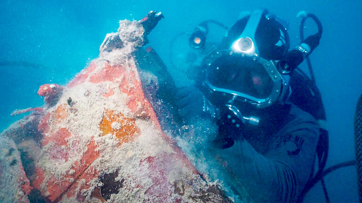A scuba diver examines a submerged World War II aircraft wreck during an underwater recovery mission.