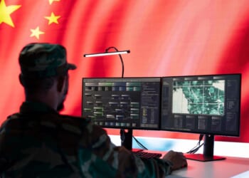 A Chinese soldier sitting at a desk, looking at a computer.