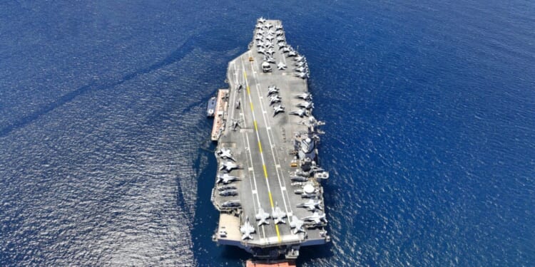 Aerial drone photo of USS Gerald R. Ford latest technology nuclear powered aircraft carrier anchored in deep blue open ocean sea.
