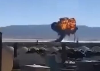 Explosion occurring in a desert landscape with smoke and flames rising against a clear blue sky.