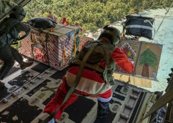 Two US soldiers throwing Christmas gifts out of the back of a cargo plane.