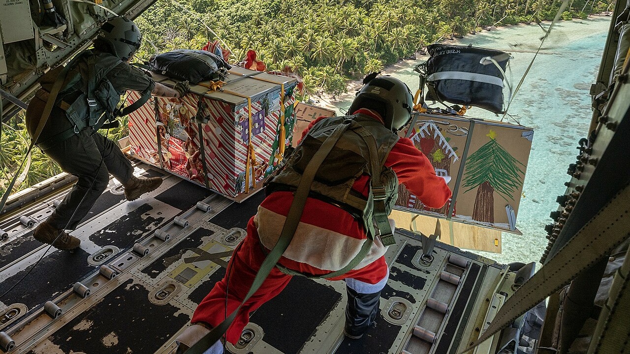 Two US soldiers throwing Christmas gifts out of the back of a cargo plane.