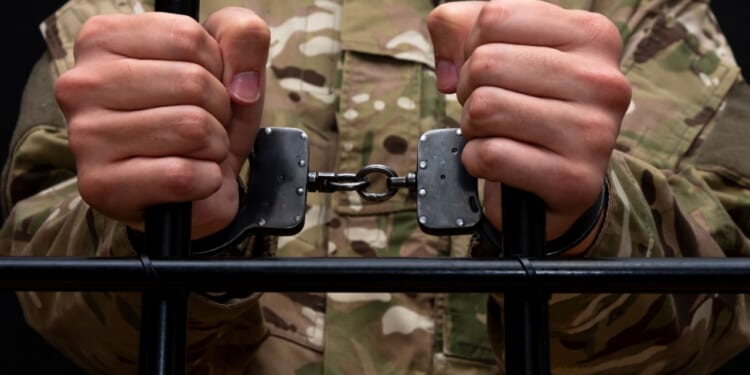 A handcuffed soldier behind the bars against a black background.