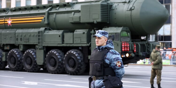 Soldiers of Russian military forces standing on background of strategic missile system "Yars" on city street, nuclear weapon.
