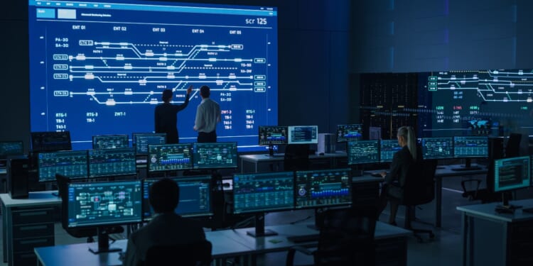 Project Manager and Computer Science Engineer Talking while Using Big Screen Display Showing Infrastructure Infographics and Data.Telecommunications Company System Control and Monitoring Room. Energy security leaders