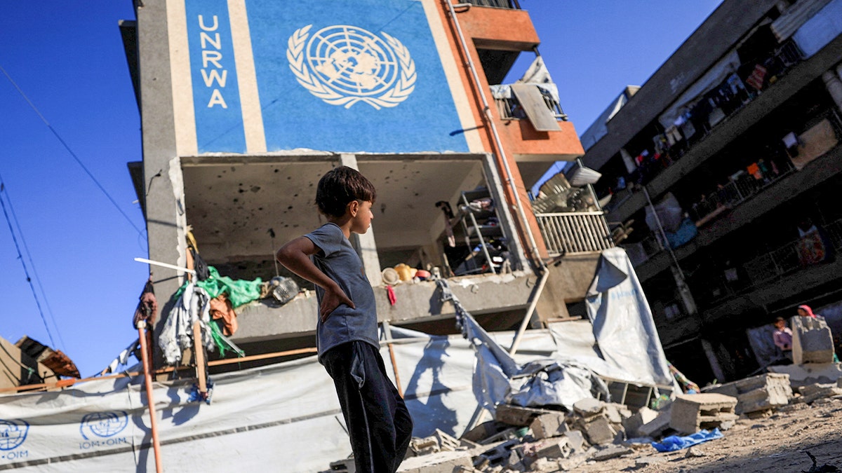 Palestinian boy walks by a building with a sign on it reading "UNRWA"