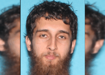 Image of a man with a beard and short, curly hair against a blue background, typically used for identification purposes.