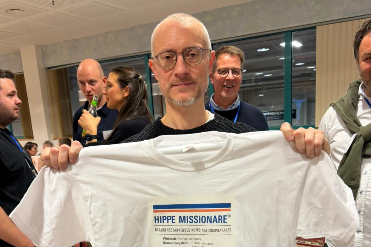 Johannes Hartl holding up a T-shirt with the ironic “hip missionary” title in reference to negative reporting in secular media during the MEHR conference in Augsburg, Germany, Jan. 3–6, 2026. | Credit: Andreas Thonhauser/EWTN