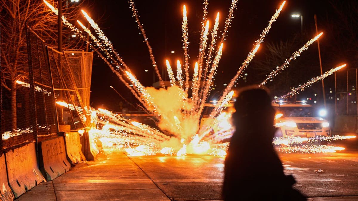 A firework explodes near fencing during a protest outside a Minneapolis federal building at night.