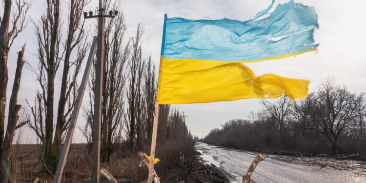 A torn Ukrainian flag flying near a road.