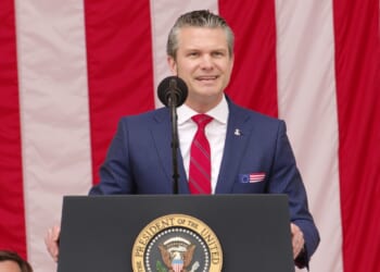 Pete Hegseth giving a speech in front of an American flag.