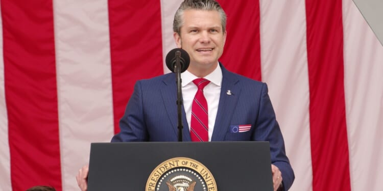 Pete Hegseth giving a speech in front of an American flag.